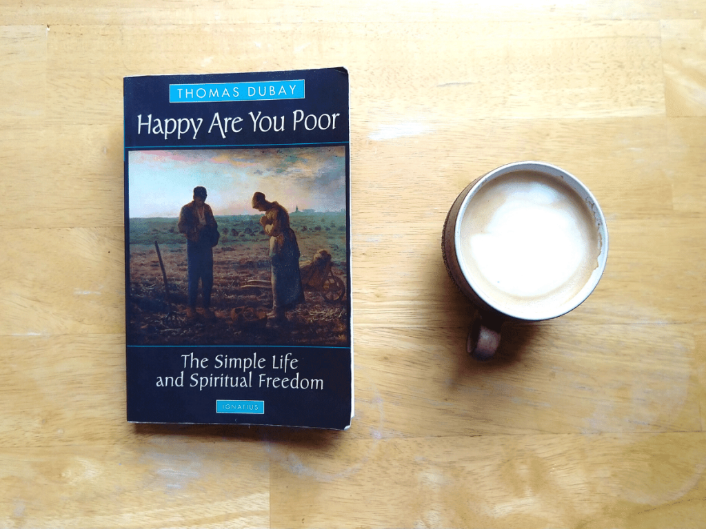book titled "Happy Are You Poor" laying on wooden table top next to small latte