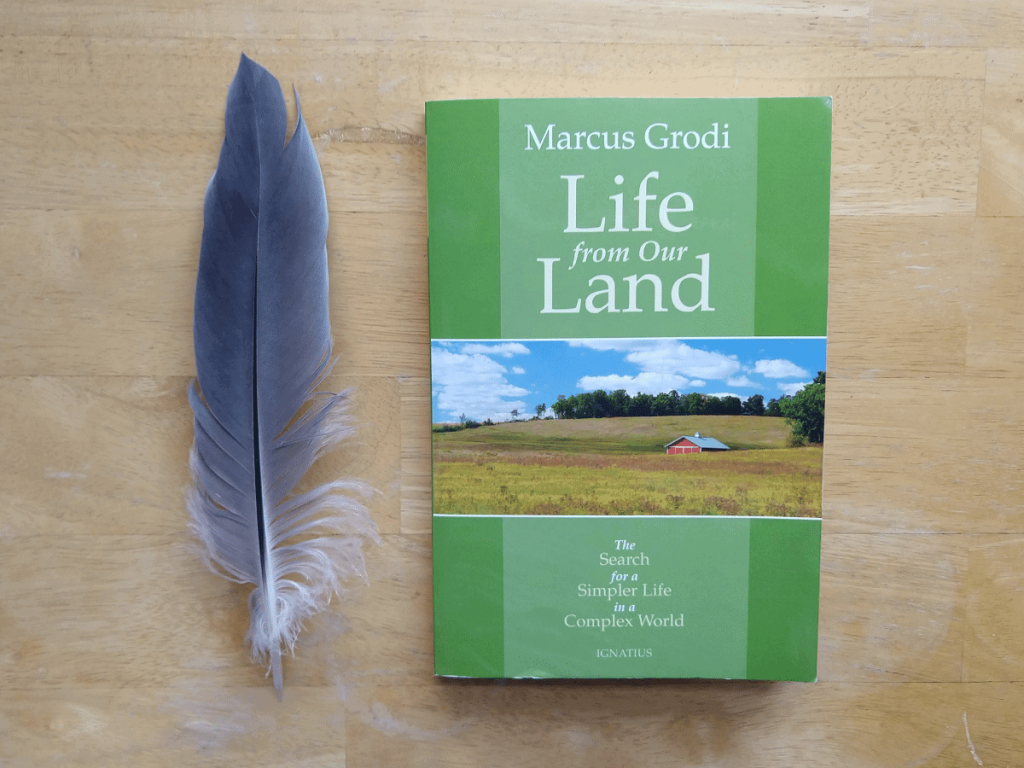 book titled "Life From Our Land" laying on wooden table top next to long grey feather